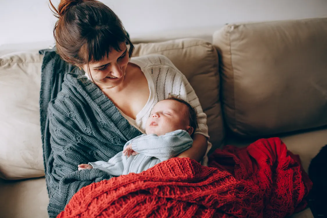 Une maman souriante berce son nouveau-né endormi sur un canapé douillet